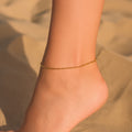 Gold anklet on a person's ankle with a blurred natural background