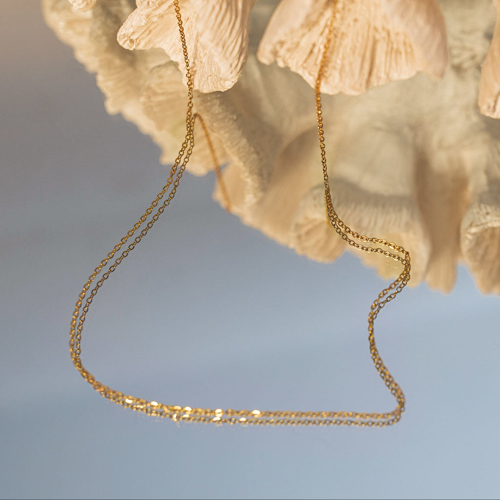 Gold chain anklet draped over a textured beige surface