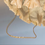 Gold chain anklet draped over a textured beige surface