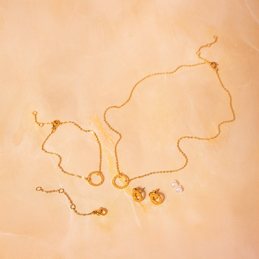 Gold necklace, bracelet, earrings, extender chain, and backings on a beige background
