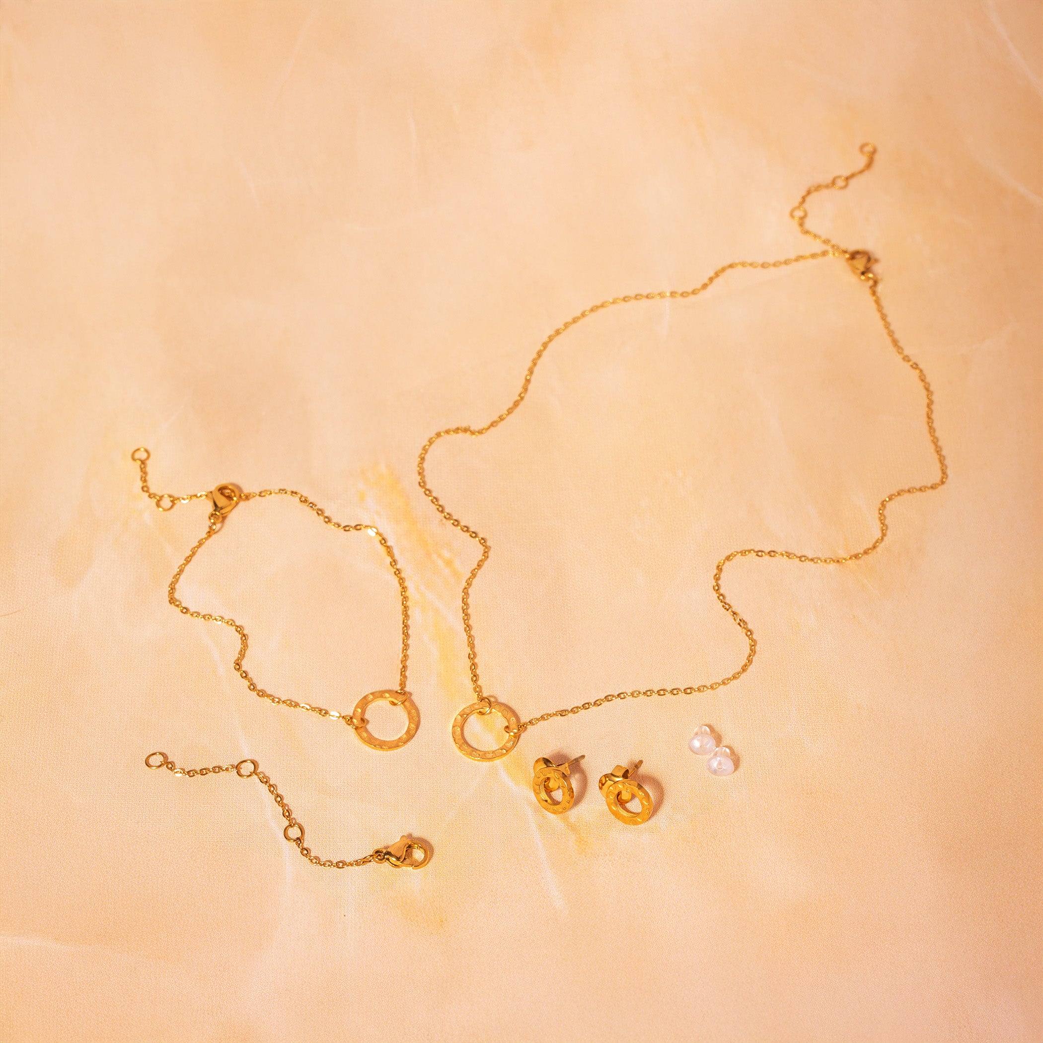 Gold necklace, bracelet, earrings, extender chain, and backings on a beige background