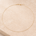 Gold necklace on a textured beige surface